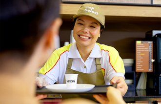 Imagem de atendente entregando um café ao cliente sorrindo